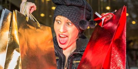 Woman with winter hat on holding up gold and red shopping bags for December holidays..