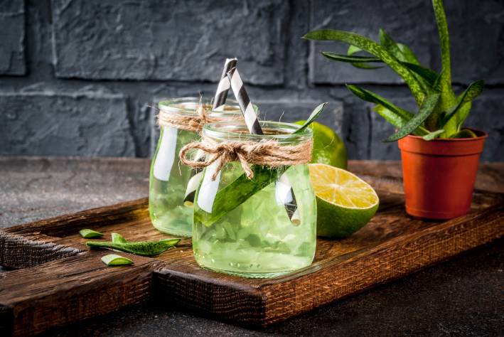 Herbal Waters & Tea Blends for Summer Aloe infused Lime water in drinking jars with black and white paper straws on a cutting board.