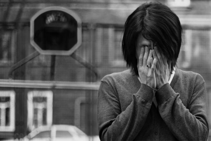 The Role of Anger in Grief Black and white image of a woman holding her hands over her face.