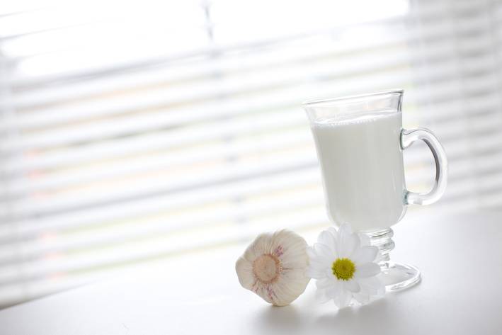 Milk as a Garlic Breath Remedy A glass of milk next to a clove of garlic and a fresh flower