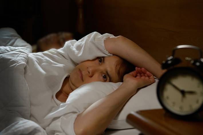 Fight Insomnia a restless woman in bed staring at the alarm clock