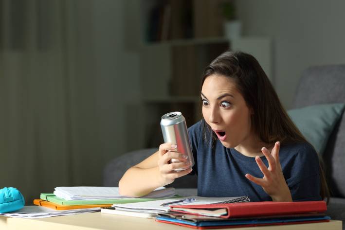 How the Top Ingredients in Energy Drinks Work a young woman studying, looking at her energy drink can in surprise