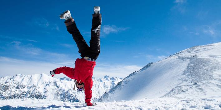 Power Up! Someone doing a one-handed handstand high in the snowy mountains
