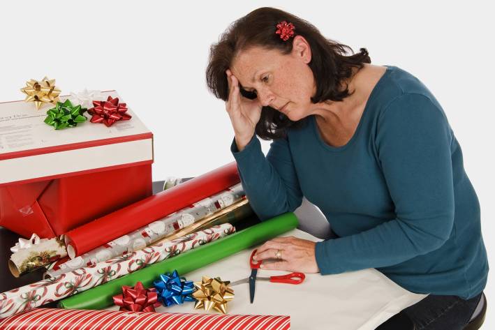 Survive Holiday Fatigue A very tired woman slouching in front of a pile of gift wrapping paper