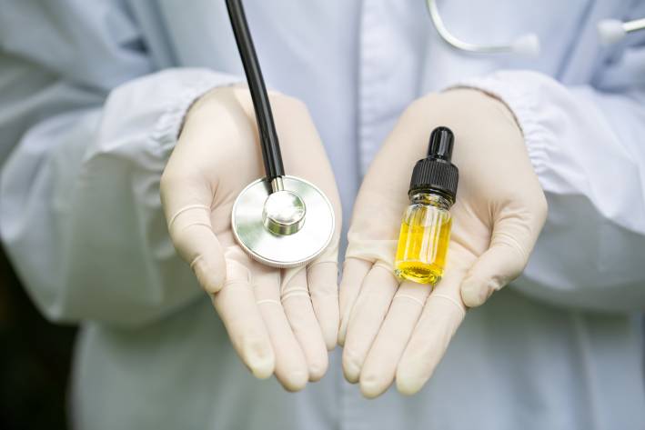 CBD May Ease Inflammation A Dr.'s hands holding a stethoscope and a bottle of CBD oil.