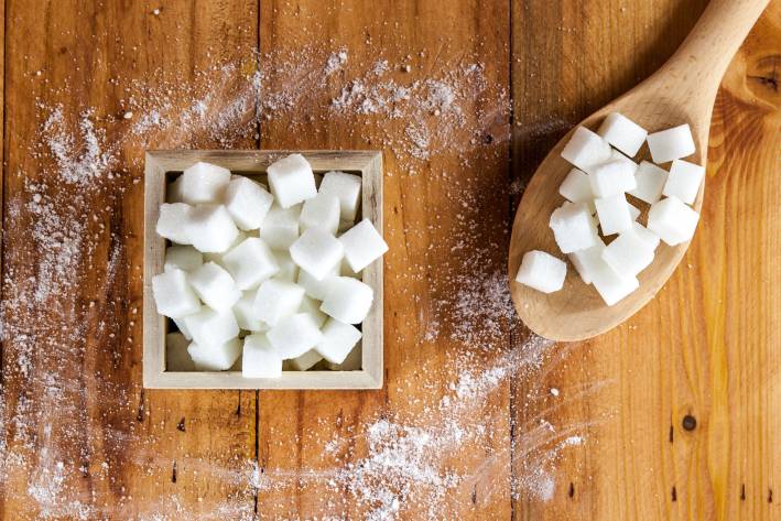 Is Your Sugar Vegan? Sugar cubes in a box next to a wooden spoon filled with sugar cubes.