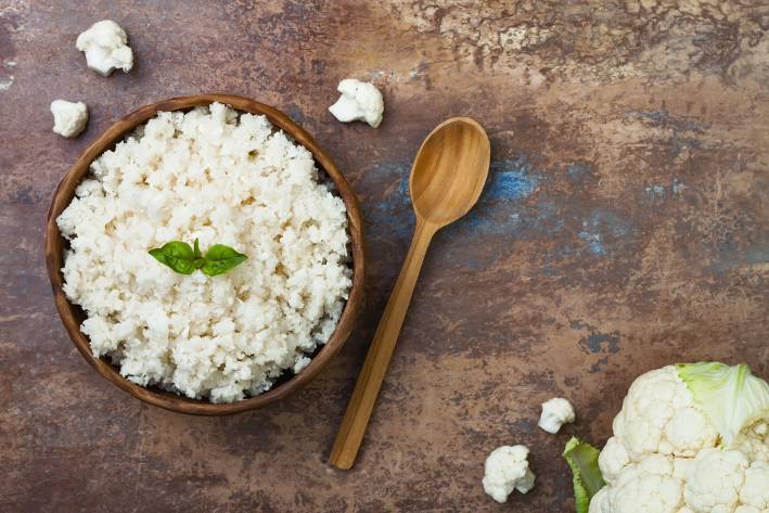 Cauliflower Rice with Zucchini, Parmesan Cheese, and Basil A wooden bowl filled with cauliflower rice.
