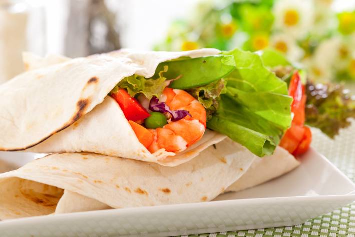 Shrimp Tacos with Tomatillo-Sunflower Salsa Verde Prepared shrimp tacos on a white plate with flowers in the background.