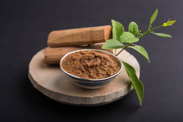Ayurvedic Anti-Acne & Anti-Aging Facemask Sandalwood paste in silver bowl with sticks and leaves on a circular stone base for creating paste.