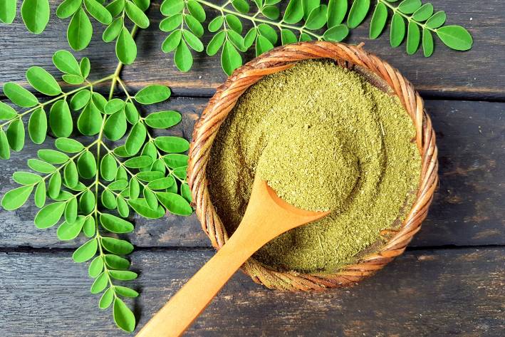 Benefits of Moringa a bowl of moringa powder and fresh leaves
