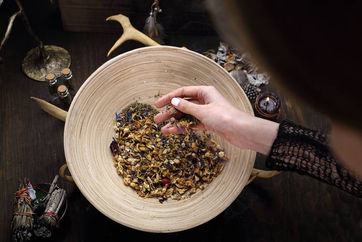 Herbalism and Spirituality a woman mixing medicinal herbs near a smudge stick and a candle