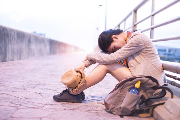 Adrenal Fatigue An exhausted woman sitting against a railing with her head on her knees