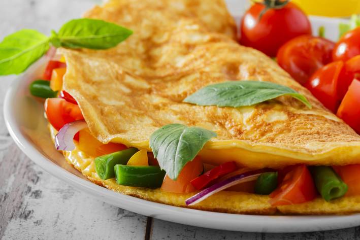 How to Cook The Perfect Omelet a perfectly-cooked omelet with veggies and chopped cherry tomatoes